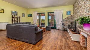 Un salon comprenant un canapé, des fauteuils, une table basse et un coin télévision avec un mur en briques et une plante en pot.