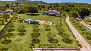 Vue aérienne d’une propriété dotée d’une piscine, d’une grande pelouse et d’une maison au toit rouge.