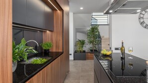 Una cocina moderna con armarios de madera, encimeras negras y una estufa empotrada. Hay plantas en macetas y un frutero sobre la encimera.