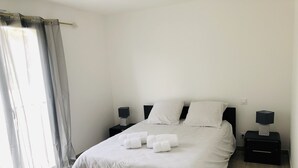 A neatly made bed with white linens and towels, two bedside tables with lamps, and a window with sheer curtains. - U PRIMU - Spacious, quiet apartment Aléria (Aléria)