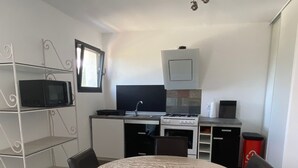 A compact kitchen with a microwave, stove, and sink. There is a dining table with chairs and a TV mounted on the wall. - U PRIMU - Spacious, quiet apartment Aléria (Aléria)