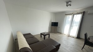 A living room with a brown sofa, a small table, a TV on a wooden stand, and a chair. - U PRIMU - Spacious, quiet apartment Aléria (Aléria)