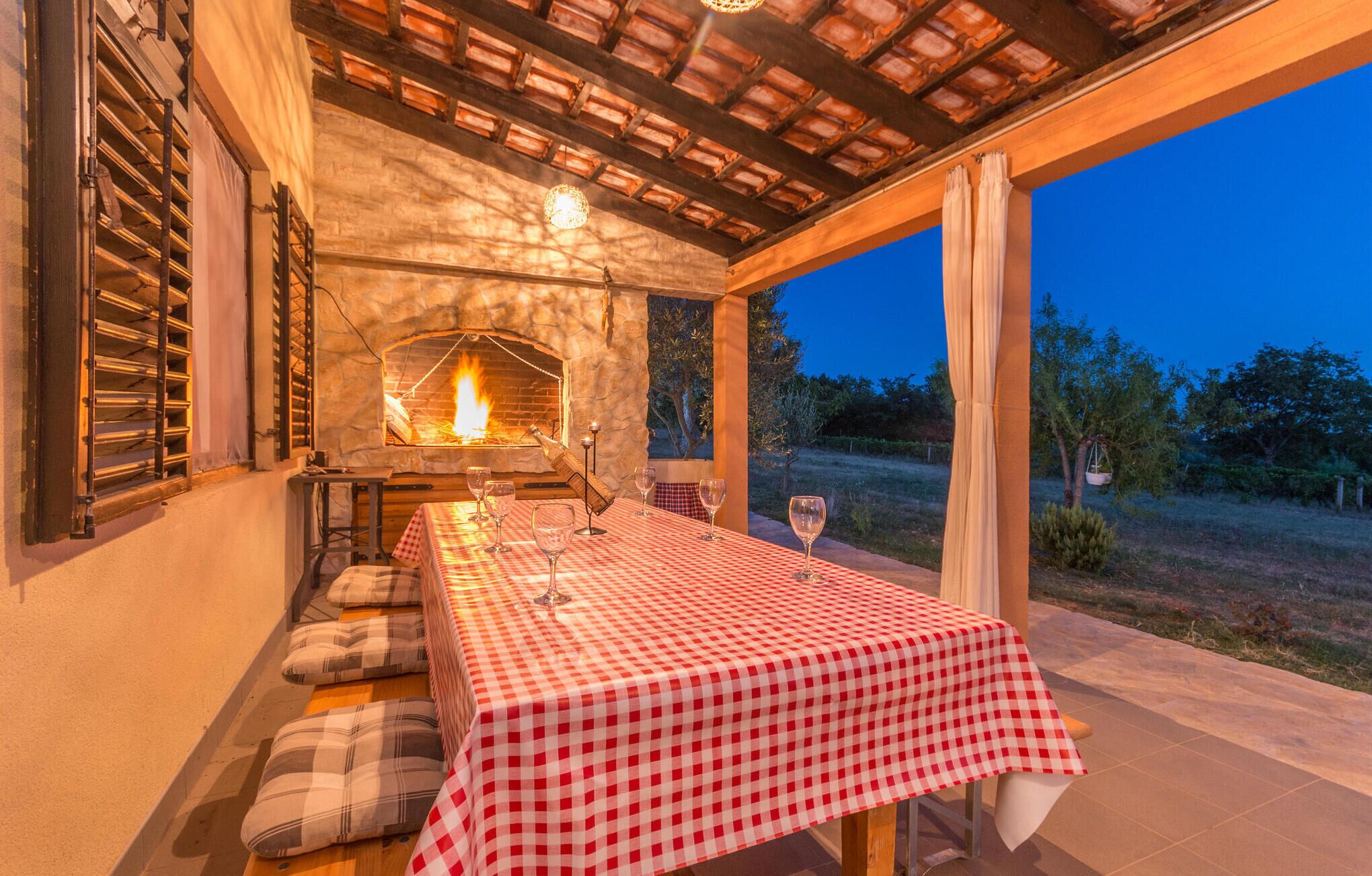 Un área de comedor al aire libre con mantel a cuadros, chimenea de piedra y vistas del paisaje circundante.