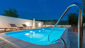 Une piscine avec un escalier en métal, des chaises longues et un mur blanc en arrière-plan.