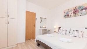 Une chambre avec une armoire en bois, une table de chevet avec une lampe, un lit avec des oreillers et un tableau floral accroché au mur.