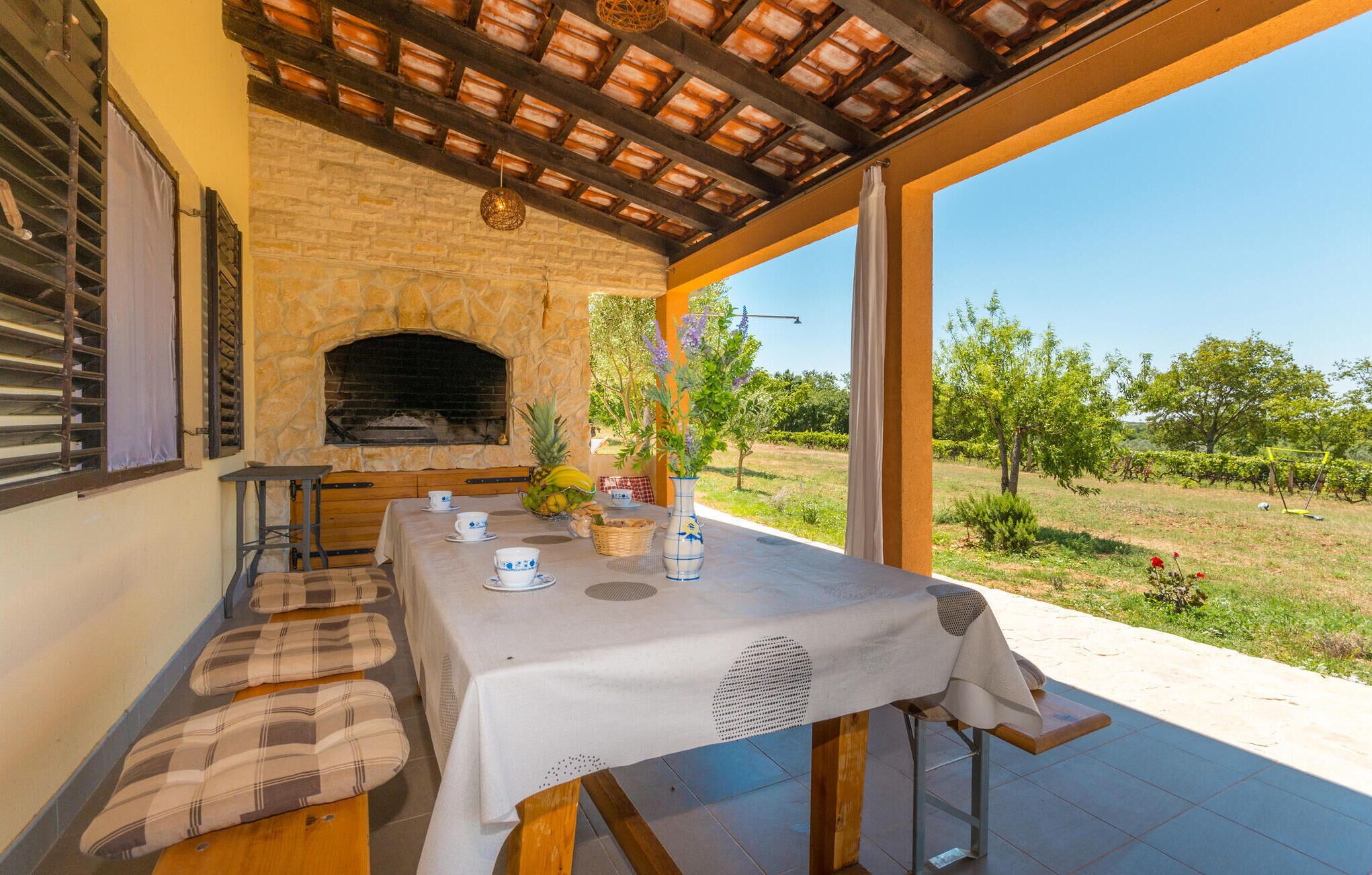 An outdoor dining area with a stone fireplace, a table set for two, and a view of a vineyard.