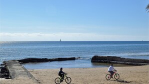 A beach with two cyclists and a sailboat in the distance. - Lovely apartment in Marina di Ragusa with WiFi (Marina di Ragusa)