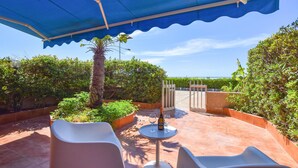 An outdoor patio with a blue canopy, two white chairs, a round table with a bottle and glasses, and a gate leading to a terrace. - Lovely apartment in Marina di Ragusa with WiFi (Marina di Ragusa)