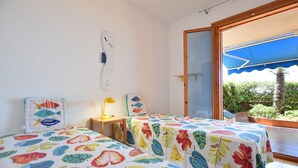 A bedroom with two beds, a small table, a lamp, and a large window with a view of greenery. - Lovely apartment in Marina di Ragusa with WiFi (Marina di Ragusa)