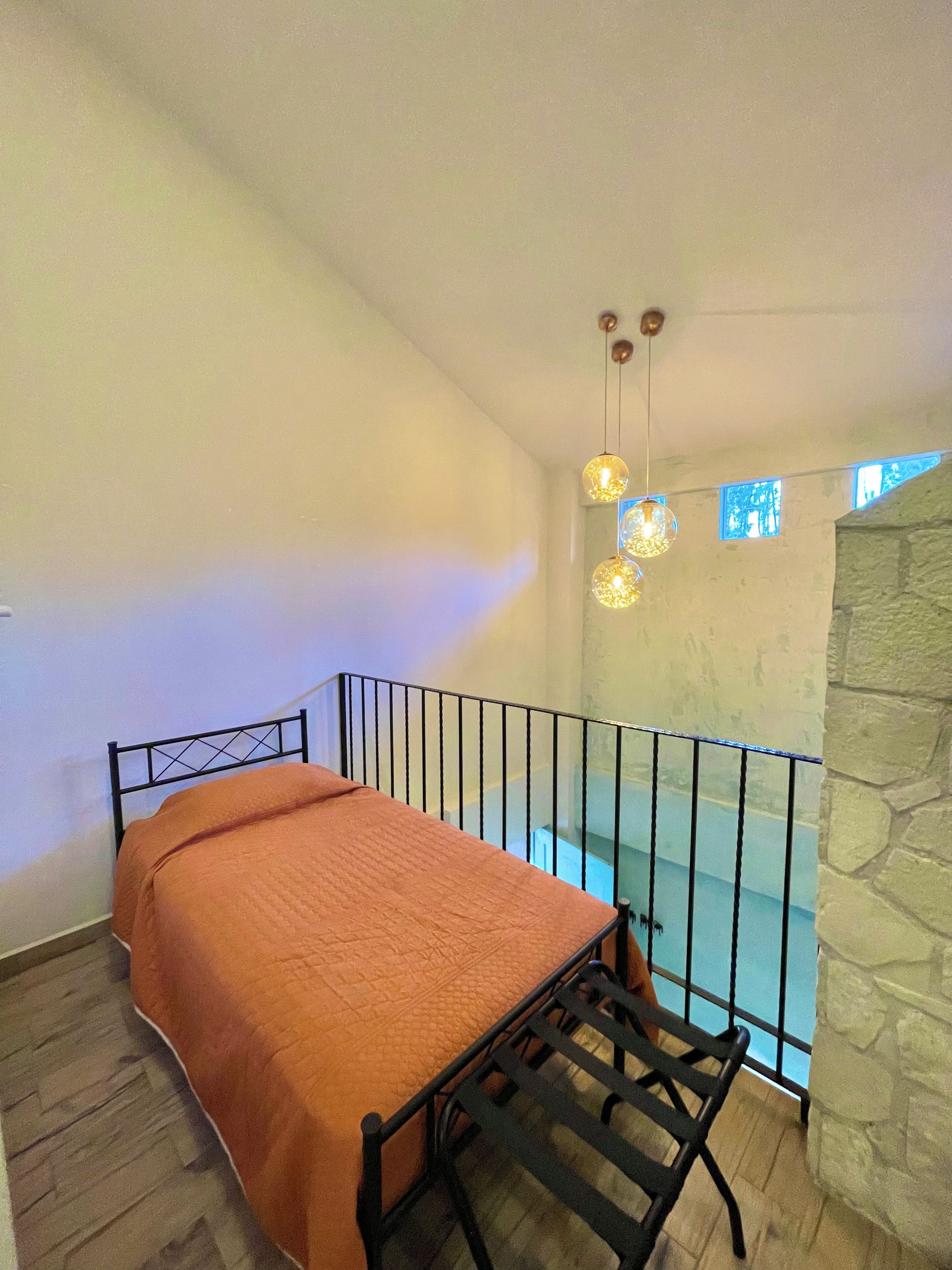 Een slaapkamer met een bed, een klein balkon met een hekwerk en een stenen muur.