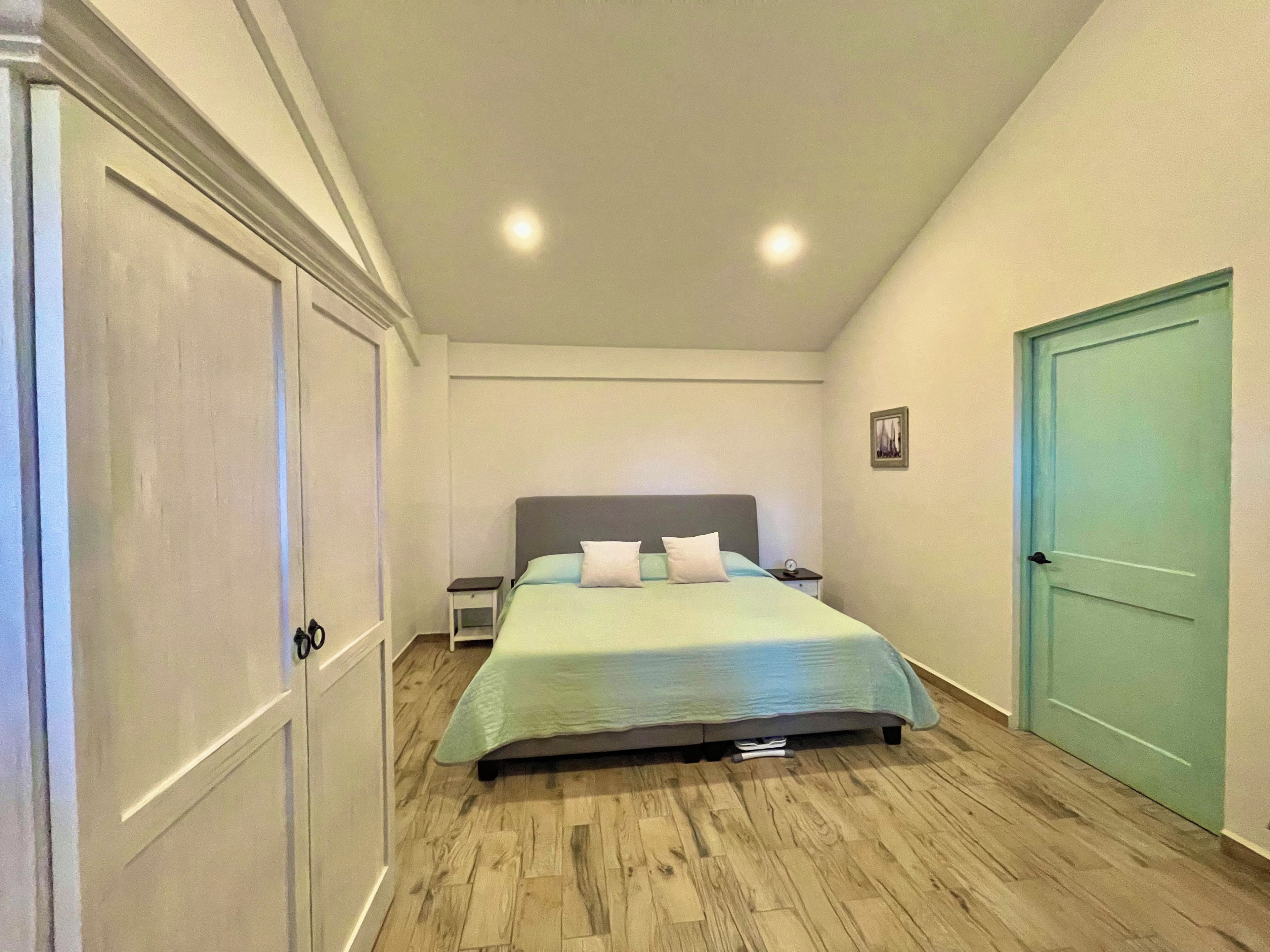 Une chambre à coucher avec un lit, des tables de chevet, une commode, une porte et un tableau au mur.