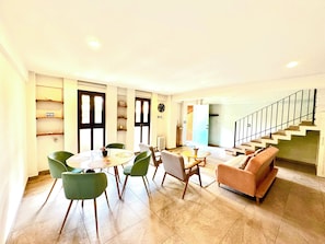 A modern living room with a sofa, chairs, a dining table, and a staircase.