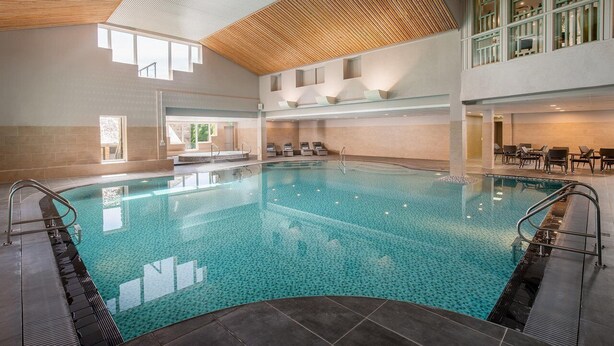 A large indoor swimming pool with clear water, surrounded by a tiled floor and walls, and a wooden ceiling. - Exceptional 3-bedroom lodge on spacious country estate. Free gym, pool & more. (Praze-an-Beeble)