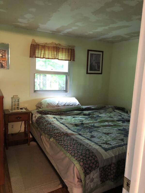 Une chambre à coucher avec un lit, une table de chevet, une fenêtre et un tableau accroché au mur.