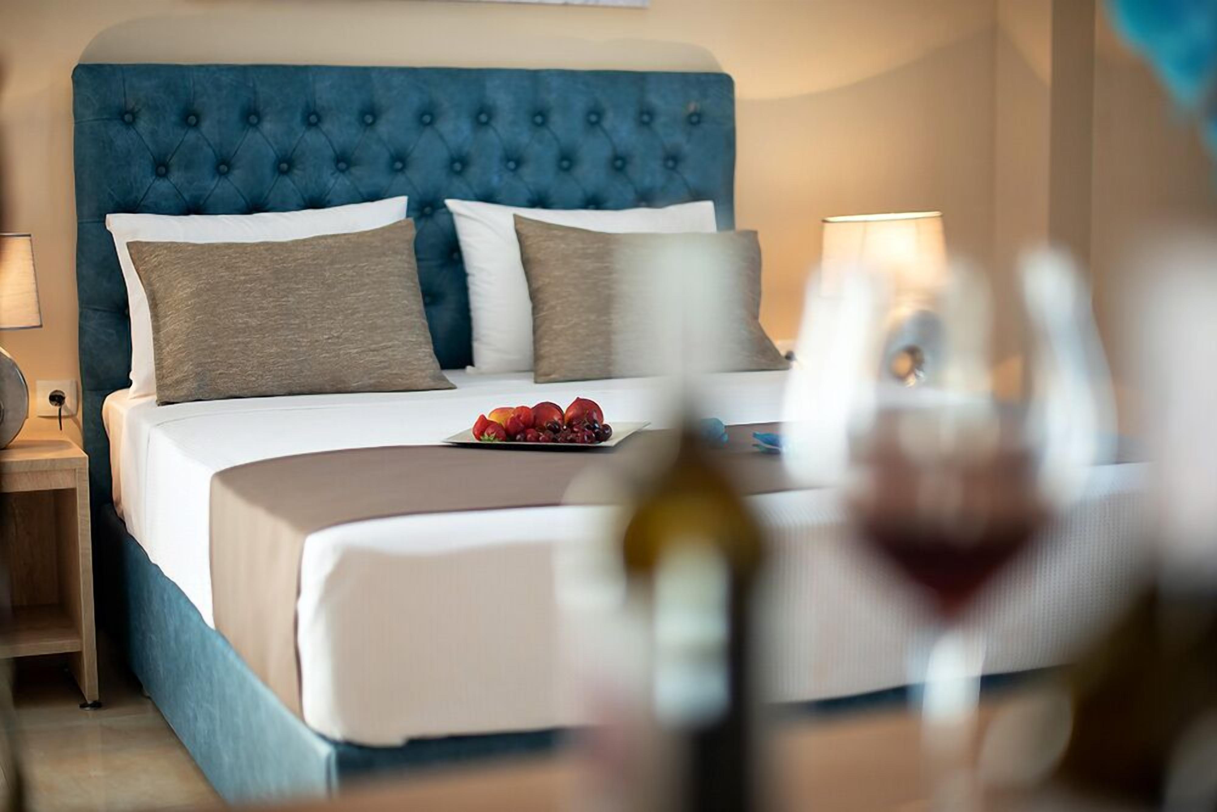 A hotel room with a tufted headboard, a neatly made bed with white linens, and a fruit plate on the bed.