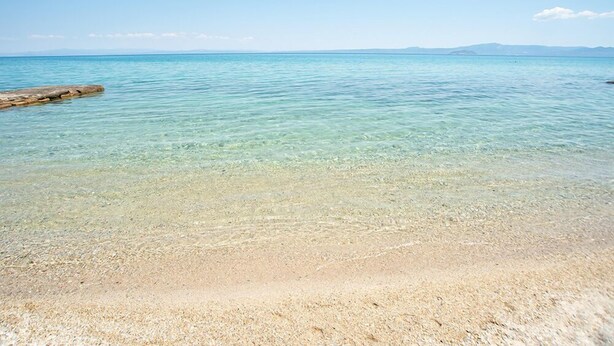 Uma praia clara com águas calmas e montanhas ao longe.