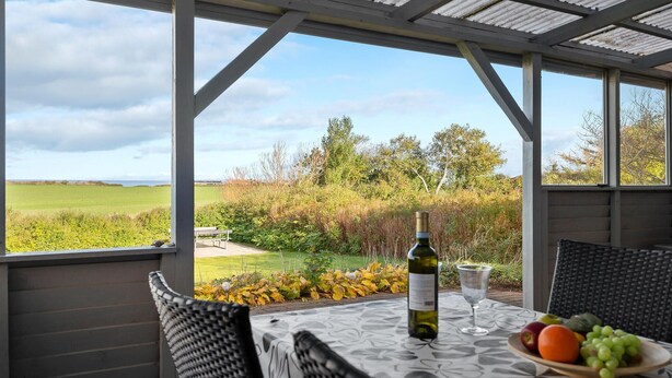 A covered patio with a table set for two, a bottle of wine, and a bowl of fruit. - Cozy home in Vinderup with WiFi (Vinderup)
