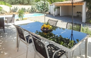Een terras met een glazen tafel, metalen stoelen en een schaal fruit.