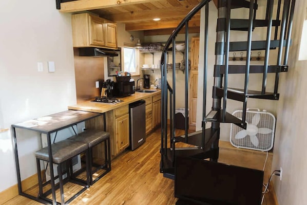 A compact kitchen with wooden cabinets, a built-in stove, and a small dining area with stools.