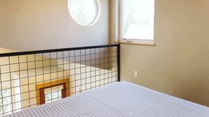 Una camera da letto con un letto, una finestra, un piccolo velux rotondo e vista sull'esterno.
