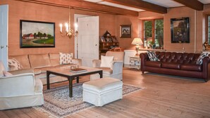 A spacious living room with a wooden floor, a brown leather sofa, a white armchair, and a beige sofa. There is a chandelier, a framed picture on the wall, and a lamp on a side table. - Beautiful home in Annelöv (Annelöv)