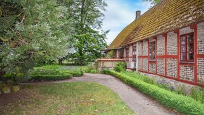 A traditional building with a red facade and a thatched roof, surrounded by lush greenery and a gravel path. - Beautiful home in Annelöv (Annelöv)