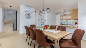 Et moderne spiseområde med et træbord og brune stole, en skål med frugt og hængende lamper.
