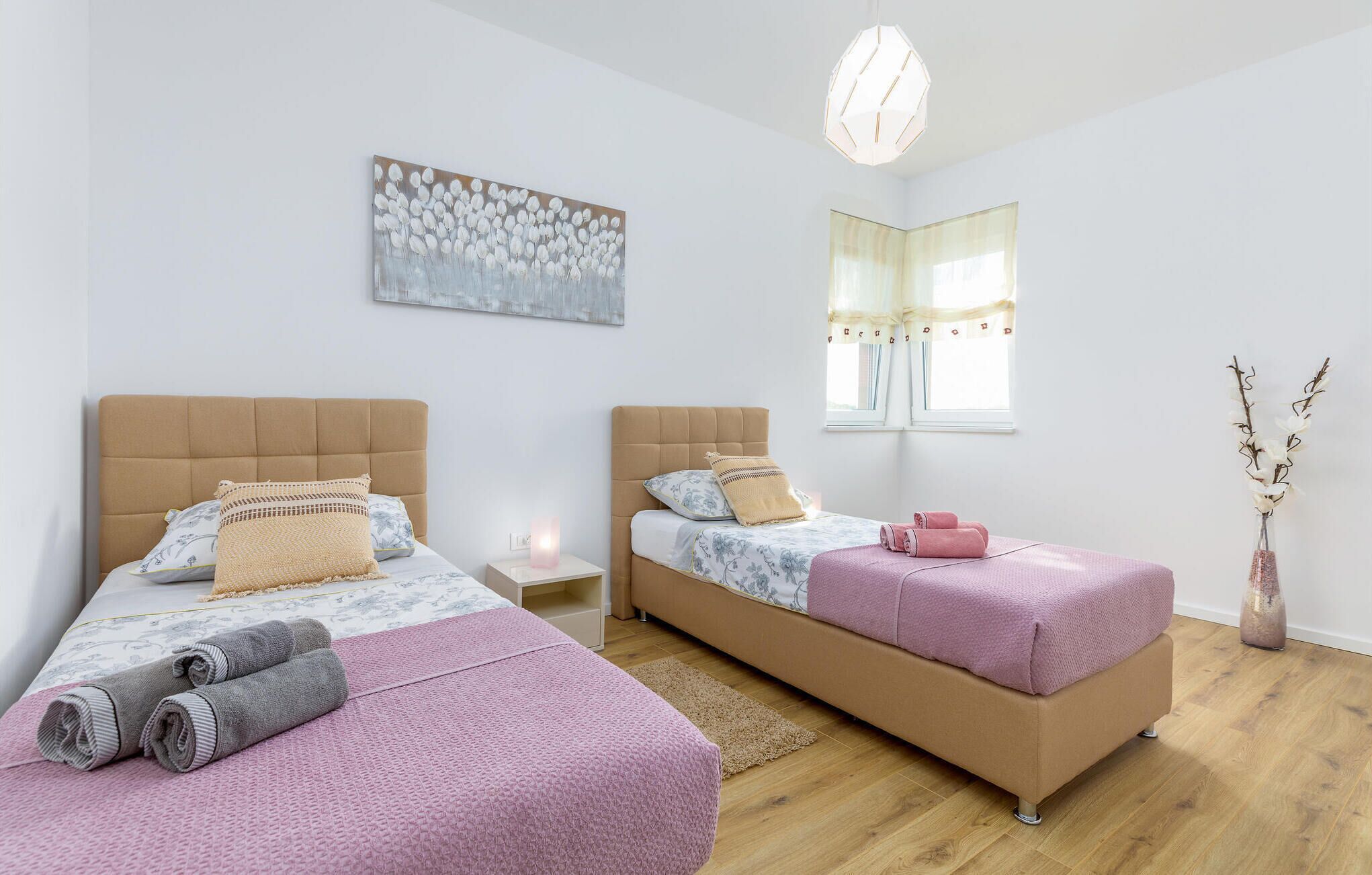 A modern bedroom with two beds, a large abstract painting, a window with curtains, and a vase with branches.