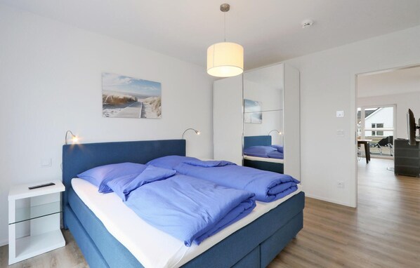 A modern bedroom with a large bed, bedside tables, a hanging light fixture, and a painting on the wall. - Pet friendly home in OstseeResort Olpenitz with sauna (OstseeResort Olpenitz)