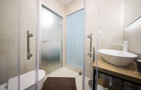A modern bathroom with a glass shower enclosure, a toilet, and a sink with a wooden countertop.