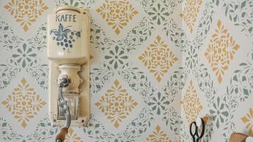 A vintage coffee grinder with the word "KAFFE" on it, mounted on a wall with a floral patterned wallpaper.