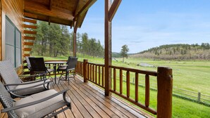 Una terraza de madera con mobiliario exterior y vistas a un campo cubierto de césped y árboles.