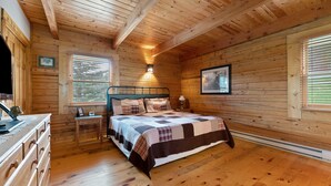 Un dormitorio de cabaña de madera con cama, cómoda, mesitas de noche y ventana.