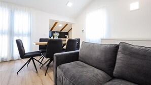 Una sala de estar moderna con un sofá gris, una mesa de comedor con sillas, y una cocina al fondo.