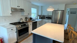 A modern kitchen with white cabinets, stainless steel appliances, a marble countertop island, and wooden flooring. - Newly built house, Central A/C, Walk to ferry, beach, and town (Tisbury)