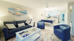Un salon moderne avec un canapé bleu foncé, une table basse en verre et un coin repas comprenant une table et des chaises blanches.