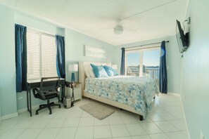 Un dormitorio con cama, escritorio, silla y vista al mar.