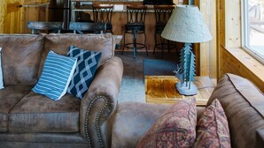 Un intérieur de chalet en bois spacieux, comprenant un coin repas, une cuisine et un espace salon confortable avec un canapé et une lampe.