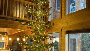L’intérieur chaleureux d’un chalet, avec un sapin de Noël décoré, des éléments en bois et un coin repas visible à travers les fenêtres.