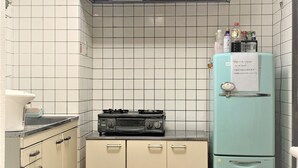 Una cocina compacta con paredes de azulejos blancos, estufa a gas, refrigerador y basurero.