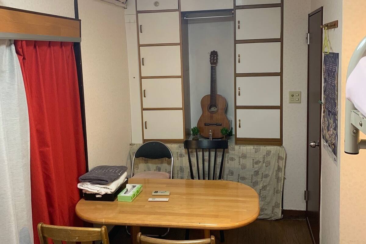 A compact room with a dining table, chairs, a guitar, and a small cabinet.