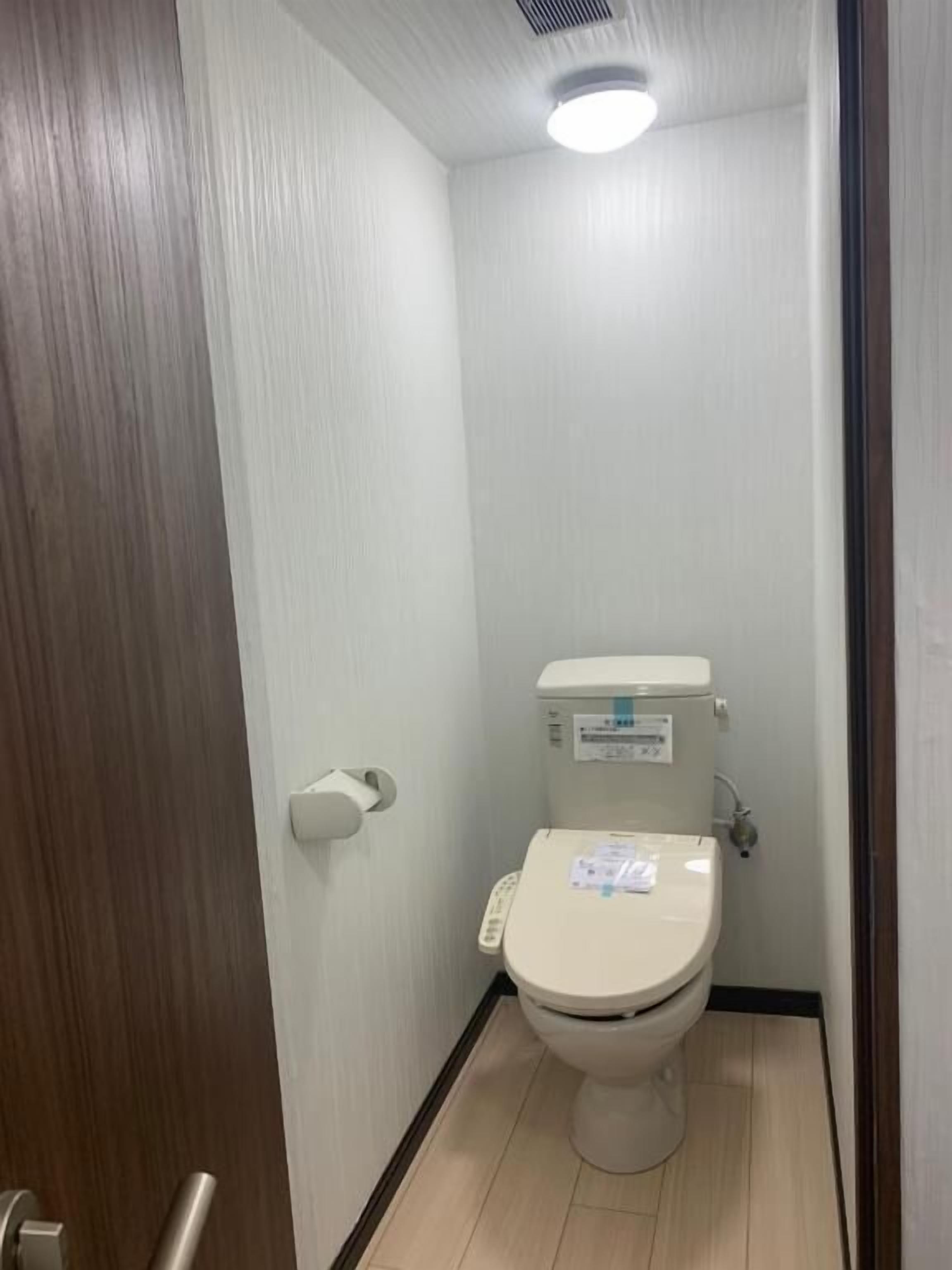 A small, narrow bathroom with a toilet, a paper towel dispenser, and a visible water heater.
