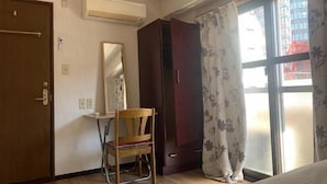 Una habitación con un escritorio de madera, una silla, un armario, un espejo y una ventana con cortinas.