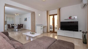 A modern living room with a flat-screen TV, a dining area with chairs, and a kitchen in the background. - Pet friendly home in Labin (Labin)