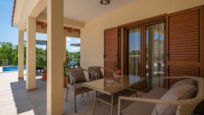 A covered patio with a glass table and wicker chairs, a pool in the background, and wooden shutters on the windows. - Pet friendly home in Labin (Labin)