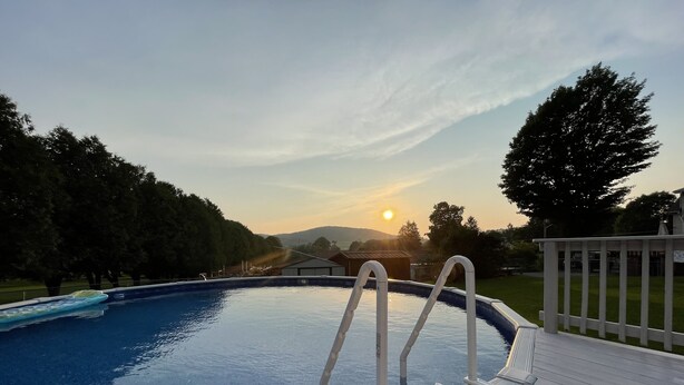A swimming pool with a wooden deck and a view of the sunset. - Cozy County Home (Richfield Springs)
