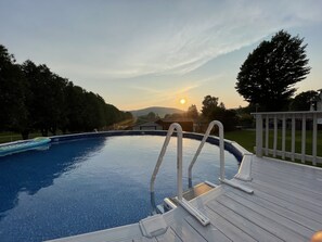 A swimming pool with a wooden deck and a view of the sunset. - Cozy County Home (Richfield Springs)