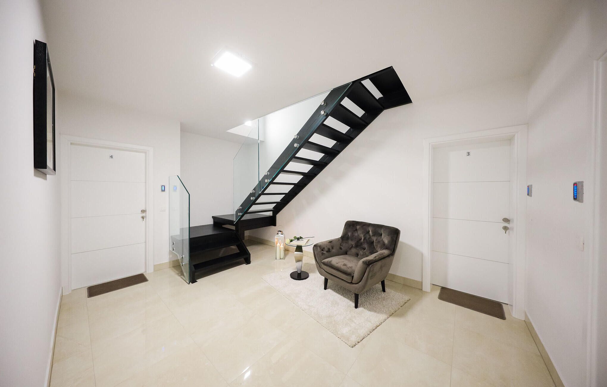 Un intérieur moderne avec un escalier en colimaçon noir, un fauteuil gris et deux portes blanches.