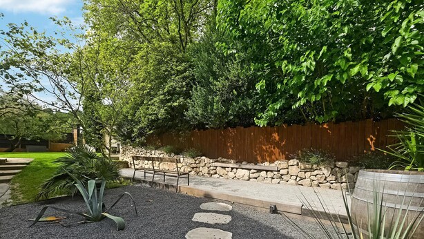 A garden with a stone wall, a wooden fence, and a gravel path with stepping stones.