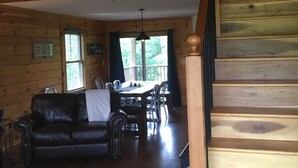 Interior de una cabaña de madera con comedor, sofá y escalera.